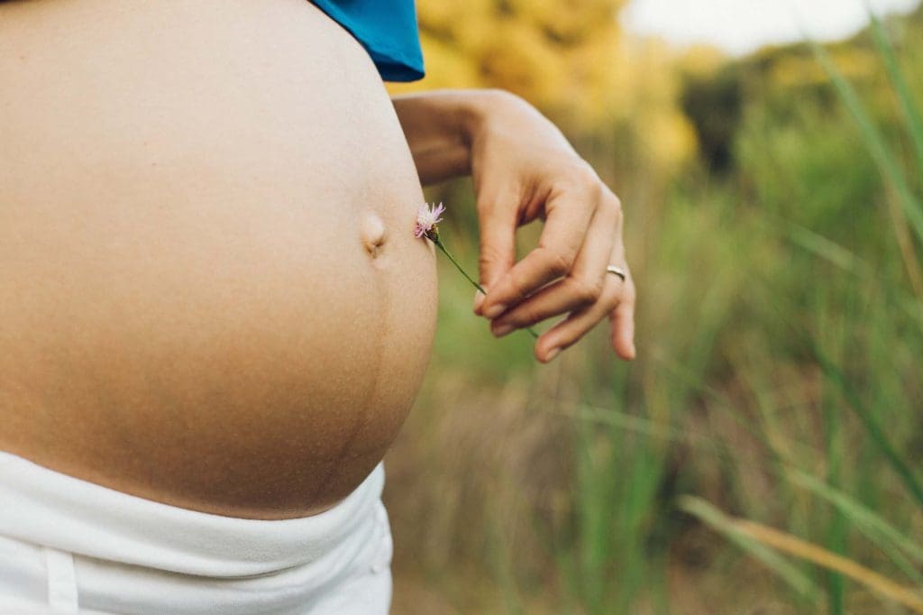 Pregnant woman holding belly while standing outdoors in nature, representing maternal health and pregnancy wellbeing care at Women’s Health Circle